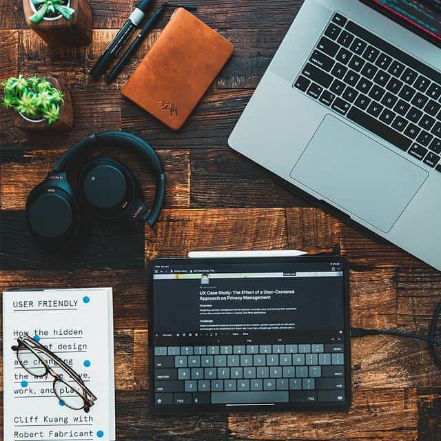 Arbeitsbereich mit Laptop, Tablet, Notizbuch und Kopfhörern auf Holz.
