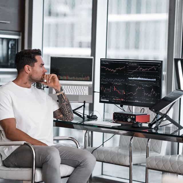 Mann beim Aktienhandel vor mehreren Monitoren mit Finanzcharts.