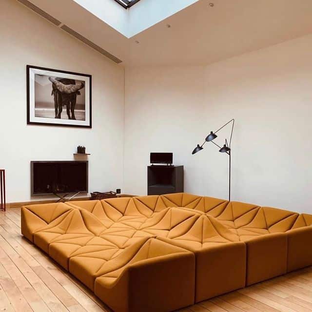 Zeitgenössisches Wohnzimmer mit orangefarbiger Sitzgruppe, Skulptur und moderner Wandkunst.