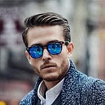 Modischer Mann mit blauen Sonnenbrillen, stilvollem Outfit und urbanem Hintergrund. Perfekt für Mode.