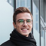 Fokko 1883, professionelles Porträt eines lachenden Mannes mit Brille vor moderner Glasfassade.