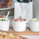 Frische Aufschnittsorten in weißen Schalen auf Holzplatte, ideal für Sandwiches und Snacks.