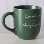 Weihnachtstasse mit Gruß "We wish you a Merry Christmas" in weißer Schrift, grüner Keramik, festlich.