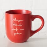 Ein roter Kaffeetasse mit weißem Schriftzug "Morgen Kinder wird's was geben" auf weißem Hintergrun.
