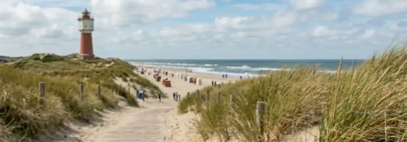 Leuchtturm an der Nordseeküste mit Sandstrand und Dünen im Hintergrund.